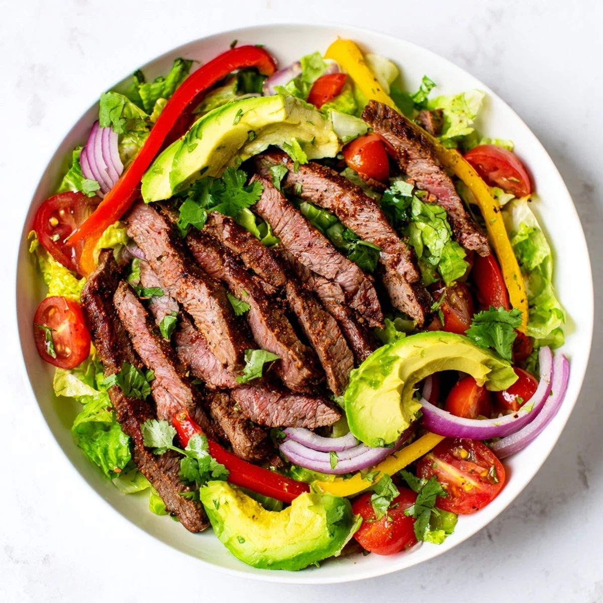 A plated Beef Fajita Salad features seared beef strips, crisp peppers, and creamy avocado over romaine with lime dressing.