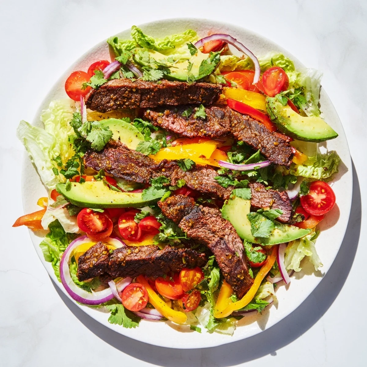 This Beef Fajita Salad highlights marinated beef, crunchy vegetables, and fresh avocado slices finished with zesty lime dressing.