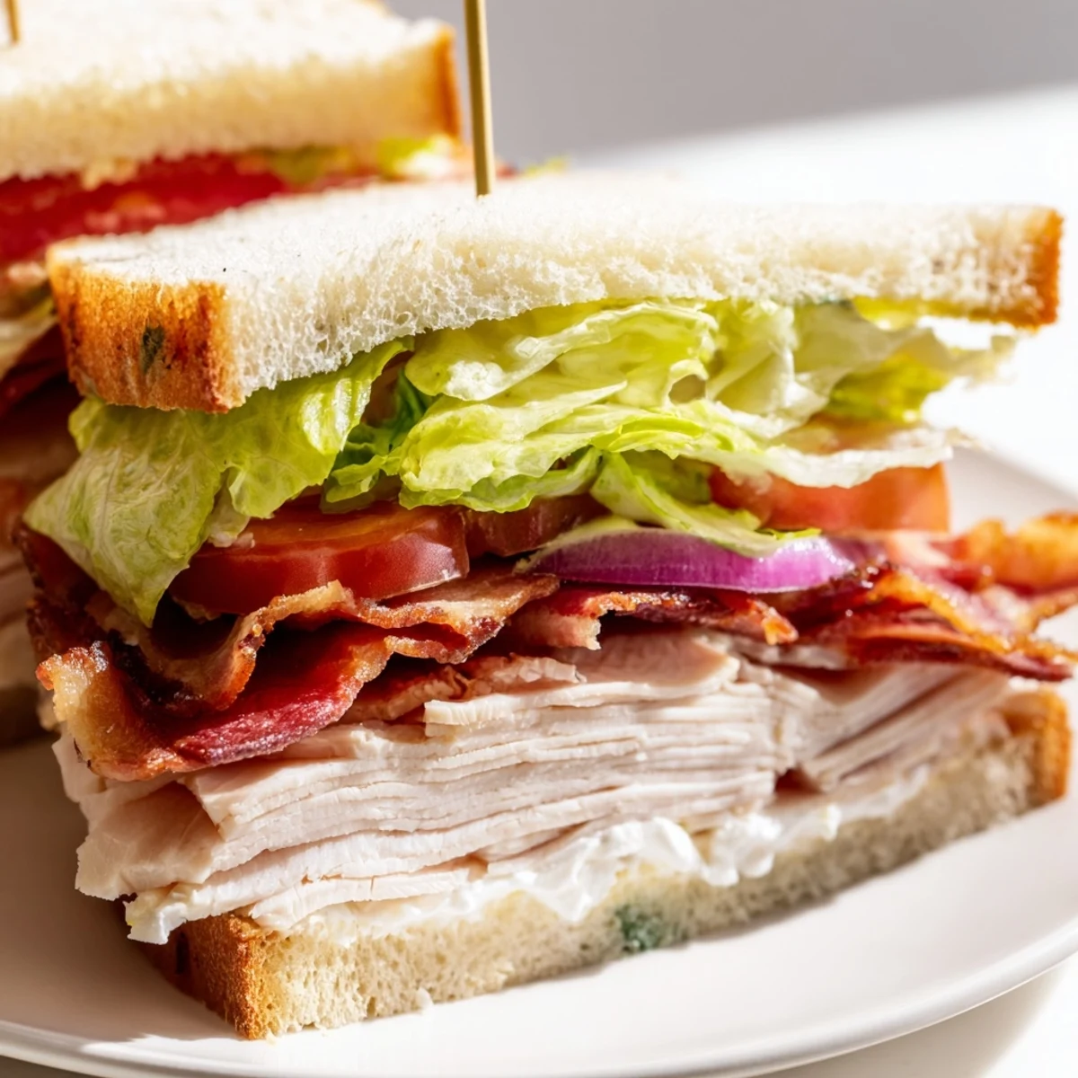 Freshly assembled Turkey Club Sandwich with turkey bacon and turkey breast, garnished with lettuce and tomato, perfect for a hearty snack or dinner.