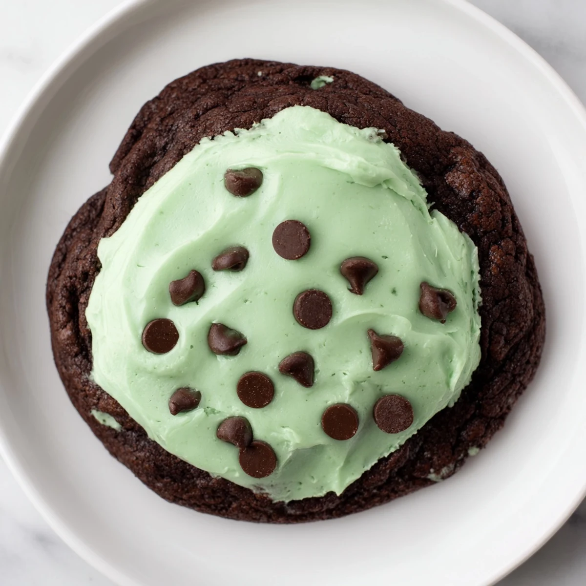 Freshly frosted Chocolate Mint Cookies with creamy green topping are arranged on a white ceramic plate for serving.