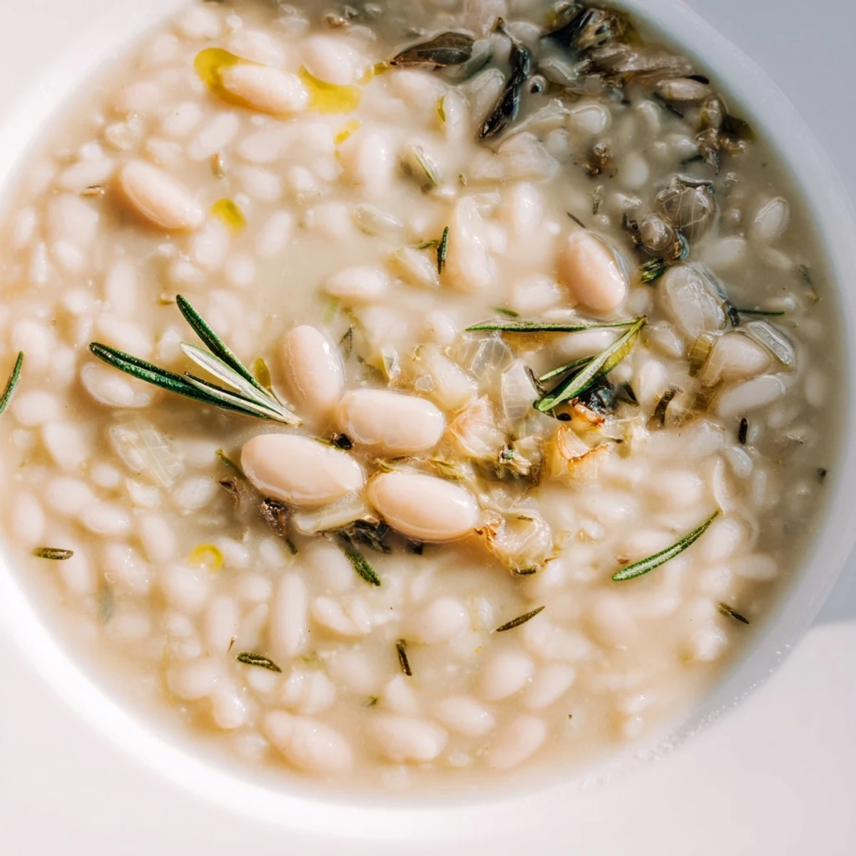 A spoon dips into the creamy Rosemary and Roasted Garlic White Bean Soup, revealing its smooth texture and chunky vegetables.
