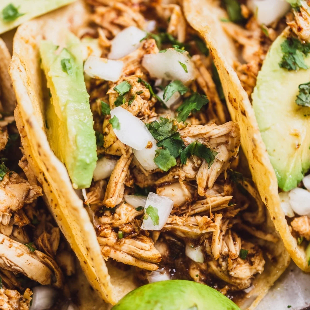 Warm, golden corn tortillas stuffed with seasoned grilled chicken, topped with fresh cilantro, diced white onion, and sliced avocado for a vibrant street-style taco night.