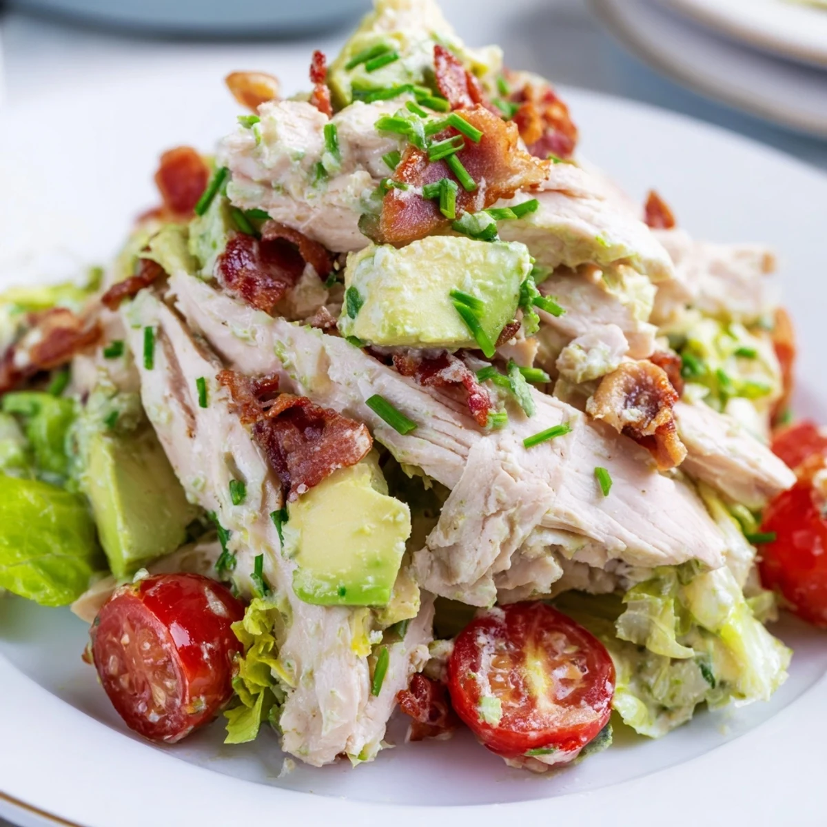 Freshly prepared BLT Chicken Salad with sliced grilled chicken, crispy bacon crumbles, halved cherry tomatoes, and creamy avocado on chopped romaine lettuce.