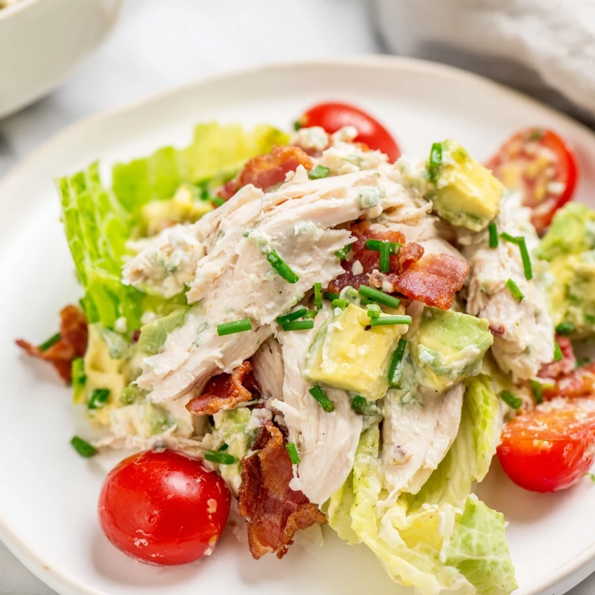 Juicy BLT Chicken Salad served in a rustic white bowl, featuring crunchy bacon, diced avocado, and a drizzle of tangy mayonnaise Greek yogurt dressing.