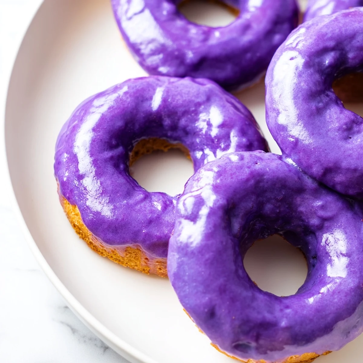 Warm Ube Mochi Donuts arranged in a ring shape, topped with glossy purple icing and a sprinkle of sugar.