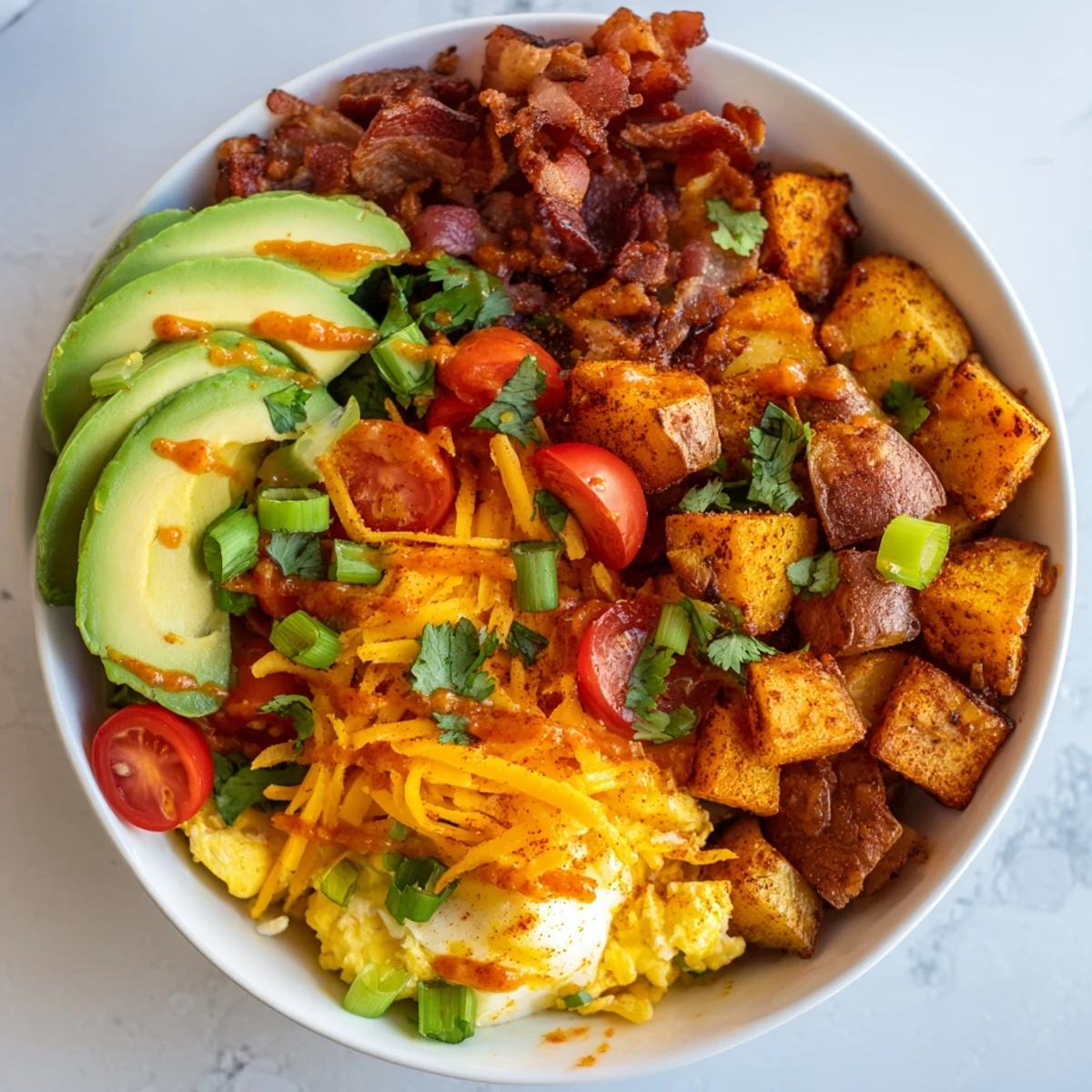 Scrambled eggs and crispy bacon sit atop roasted potatoes in a Loaded Breakfast Bowl with green onions and hot sauce.