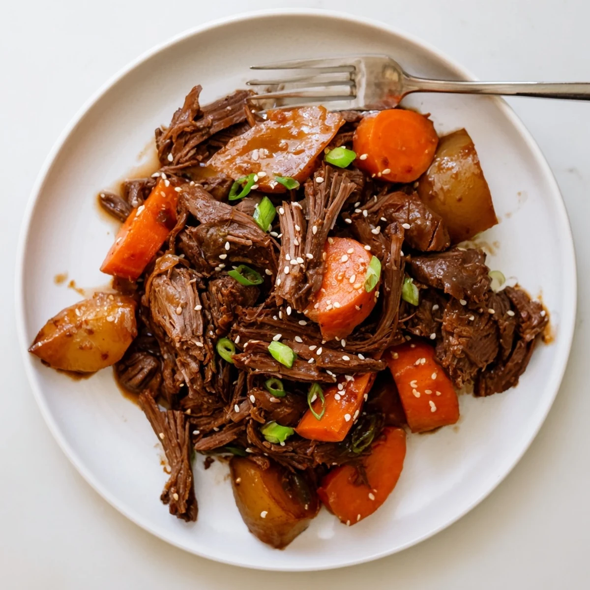 A close-up of Korean Style Pot Roast, tender shredded beef with carrots and daikon in a glossy sauce on a platter.