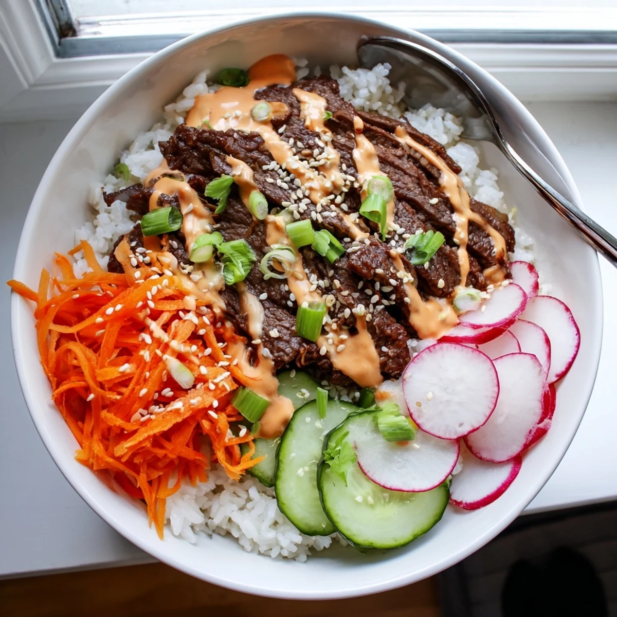 Tender Korean BBQ-marinated steak on rice topped with carrots, cucumber, radishes, spring onions, and sesame seeds.