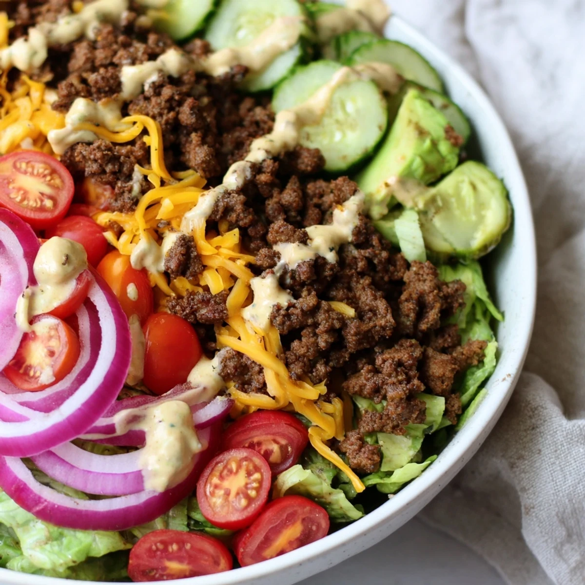 Low-carb burger bowl layered with ground beef, avocado, tomatoes, and tangy pickles