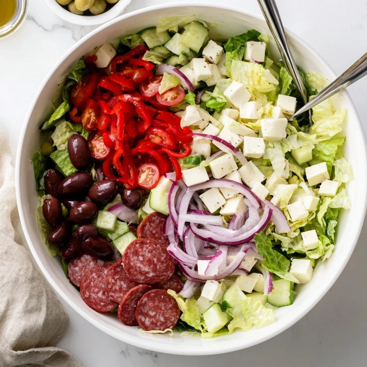 Colorful Italian chopped salad bowl with crisp romaine, salami, olives, and mozzarella tossed in zesty homemade dressing