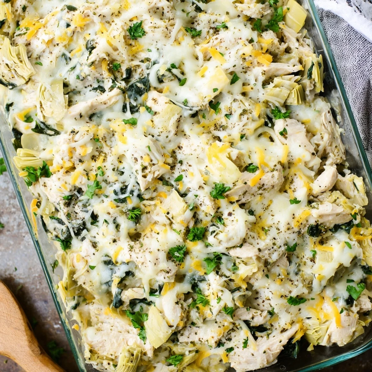 Savory baked casserole featuring shredded chicken spinach and artichokes under a layer of golden mozzarella
