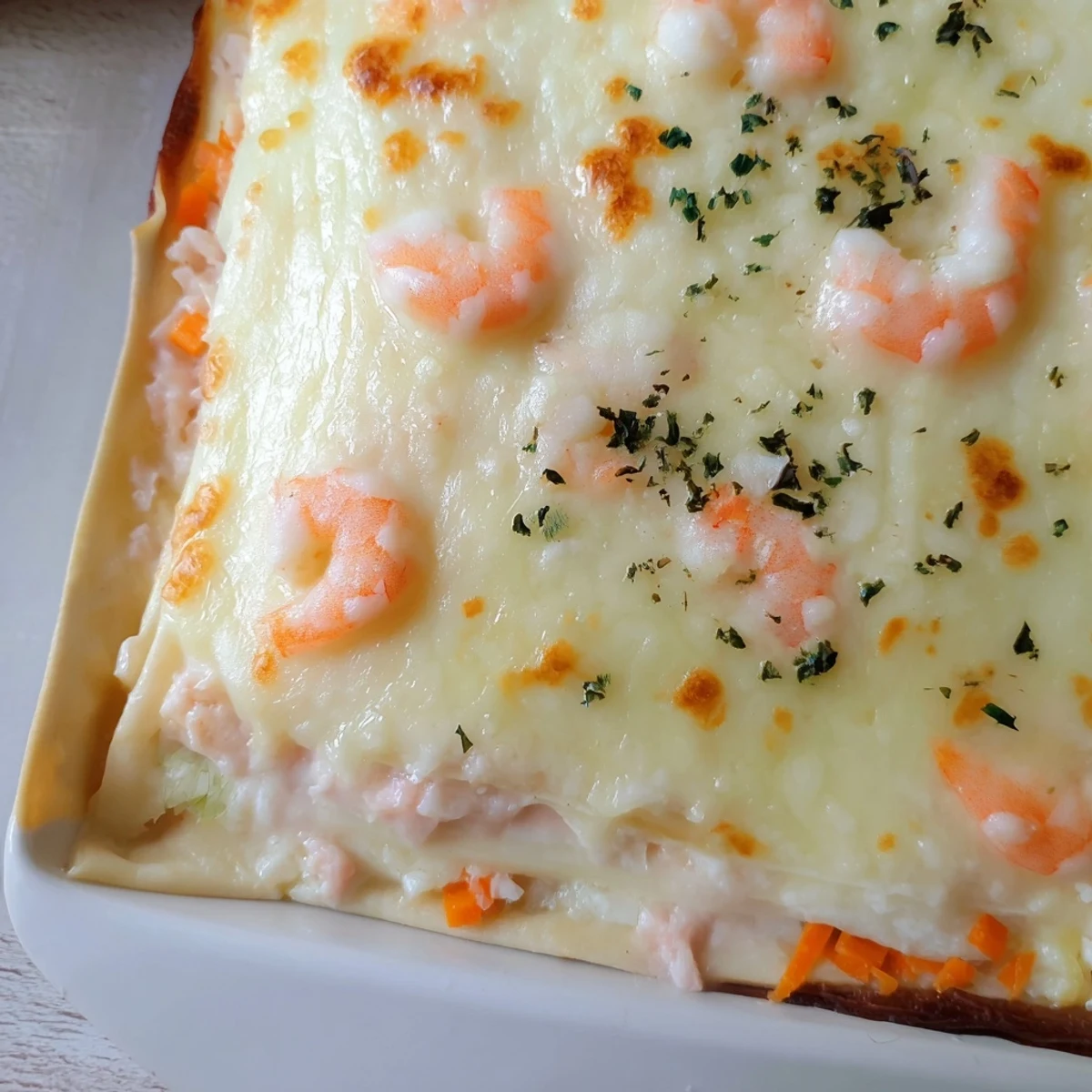 Sliced shrimp dumpling lasagna showcasing dumpling wrappers and golden cheese topping on white plate
