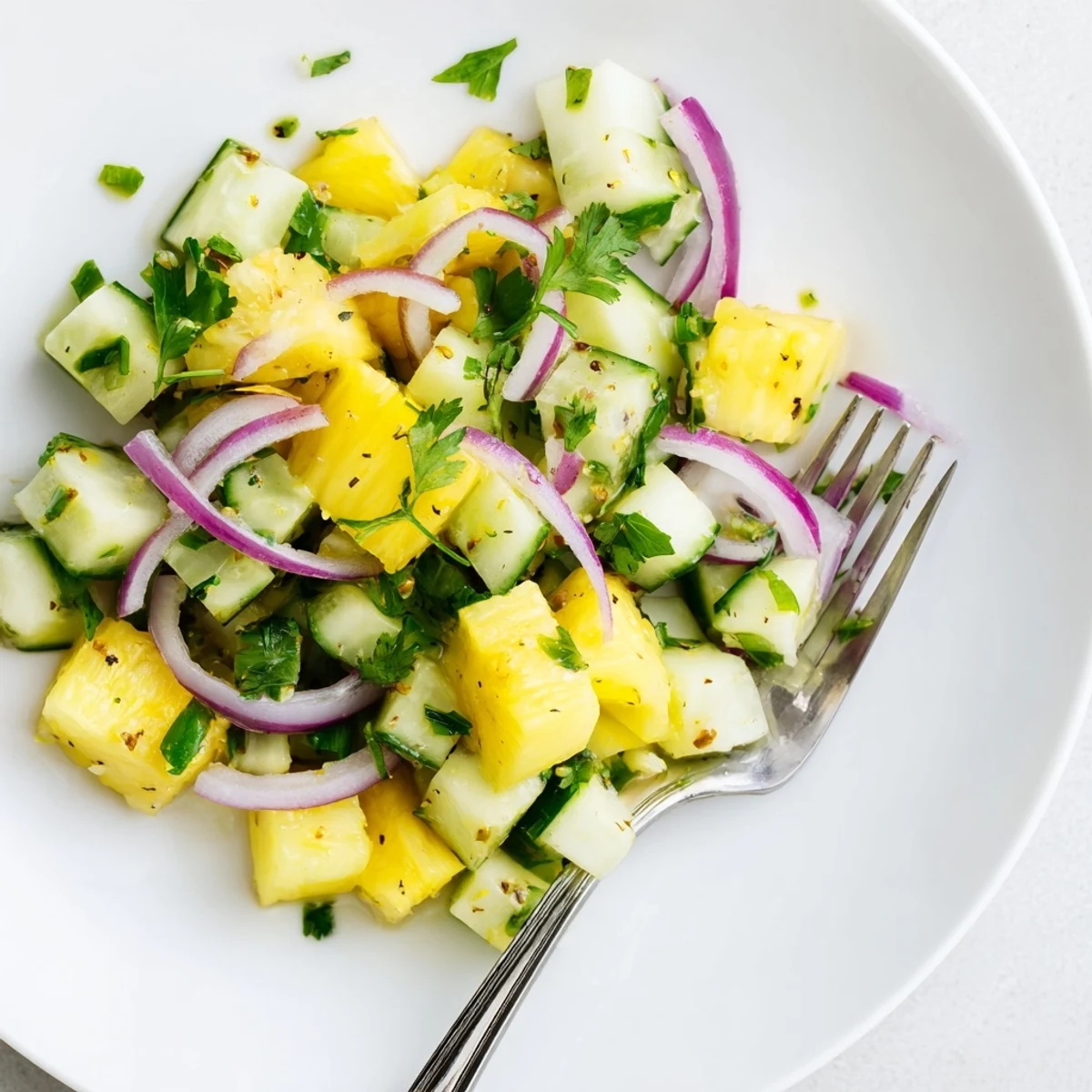 Fresh pineapple cucumber salad featuring crisp produce drizzled with zesty lime vinaigrette in white bowl