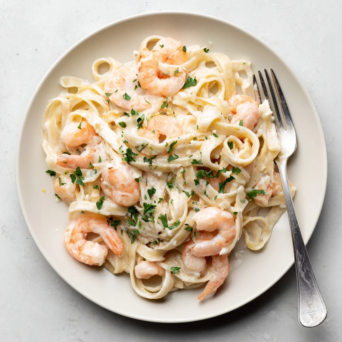 Golden brown shrimp resting on top of fettuccine Alfredo pasta in a deep skillet with fresh parsley garnish