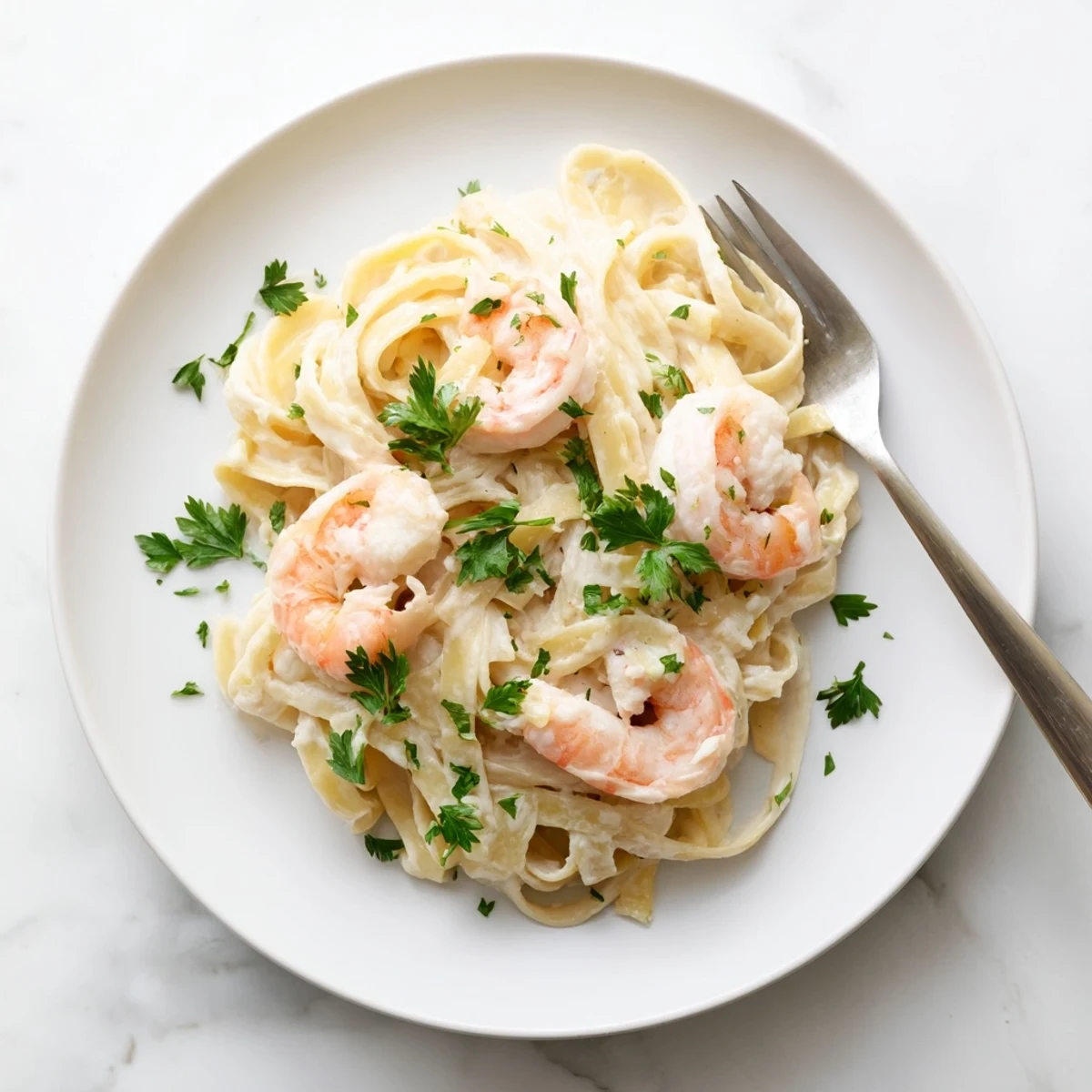 Steaming bowl of creamy shrimp fettuccine pasta with homemade Alfredo sauce and lemon wedges on white plate