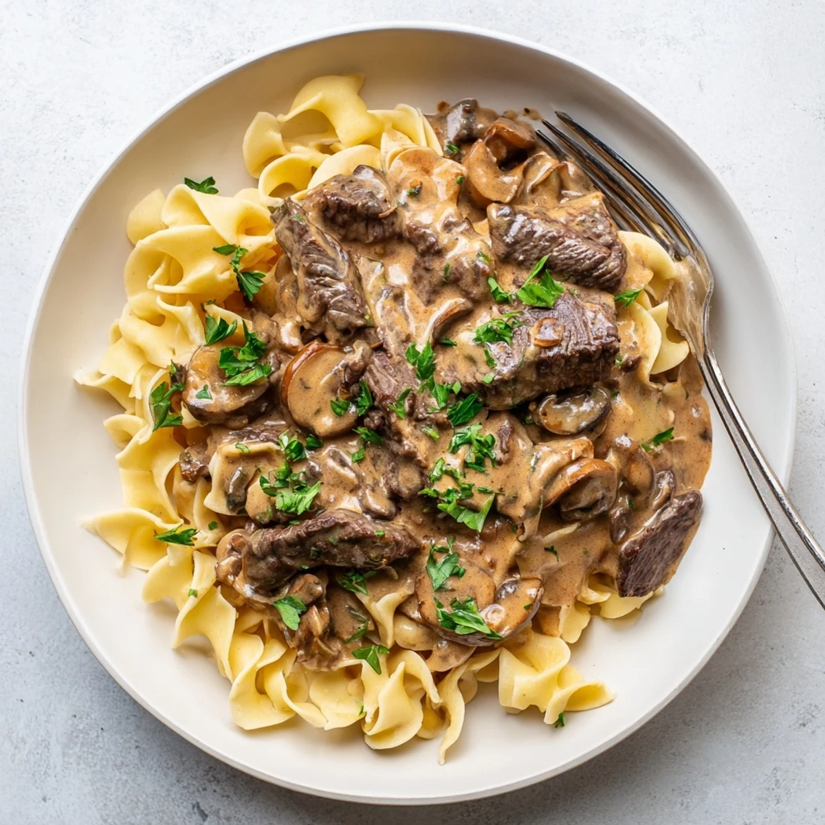 Creamy beef stroganoff served over egg noodles with fresh parsley garnish