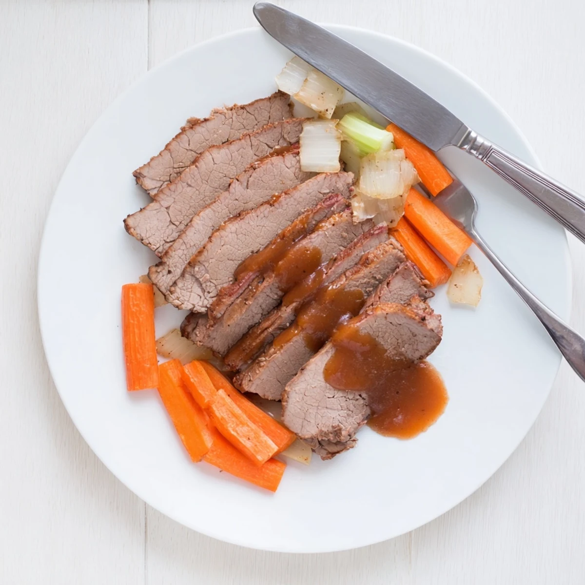 Slow cooker beef brisket with tender sliced meat served over roasted carrots and onions