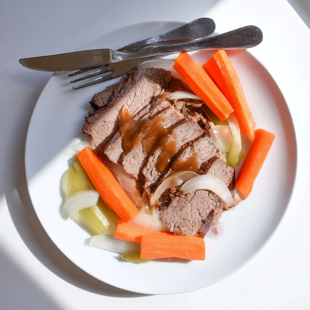 Sliced slow cooker beef brisket resting on a cutting board with caramelized vegetable medley