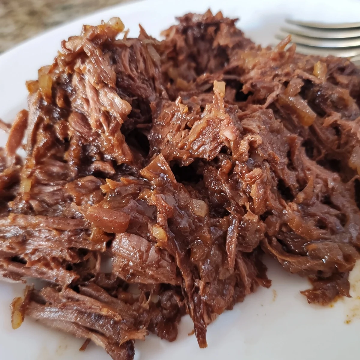 Crock Pot shredded beef piled high on a serving plate with steam rising from the shredded meat
