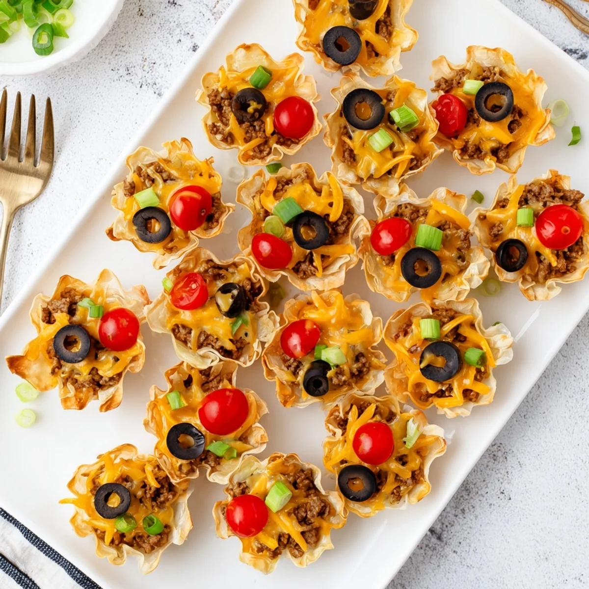 Golden Taco Ranch Bites topped with melted cheddar and fresh green onions on a serving platter