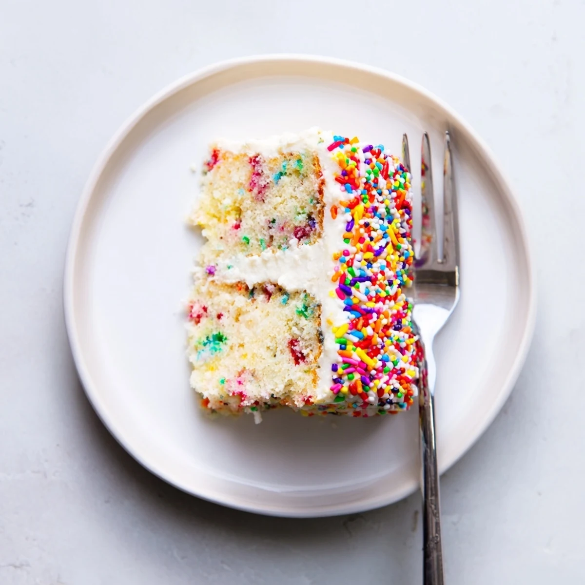 Generous slab of big batch confetti cake topped with smooth vanilla buttercream and extra rainbow sprinkles, perfect for birthday parties and gatherings