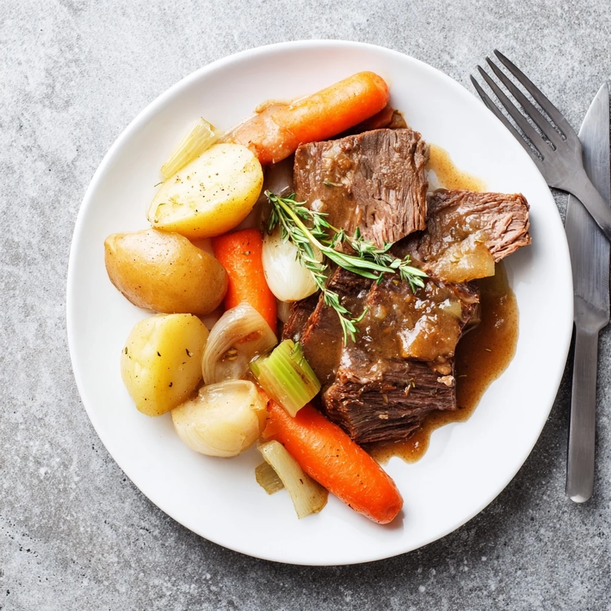 Fork-tender Southern style pot roast served with roasted vegetables and savory homemade sauce on white ceramic dinnerware