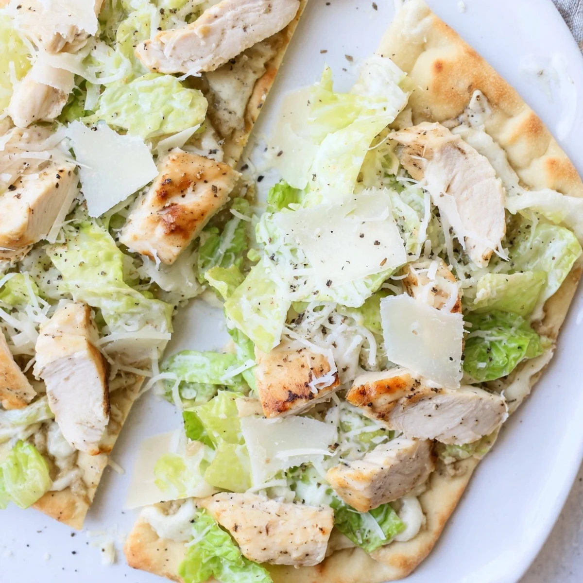 Sliced chicken breast on warm flatbread with Caesar dressing, lettuce, and bubbly melted cheese