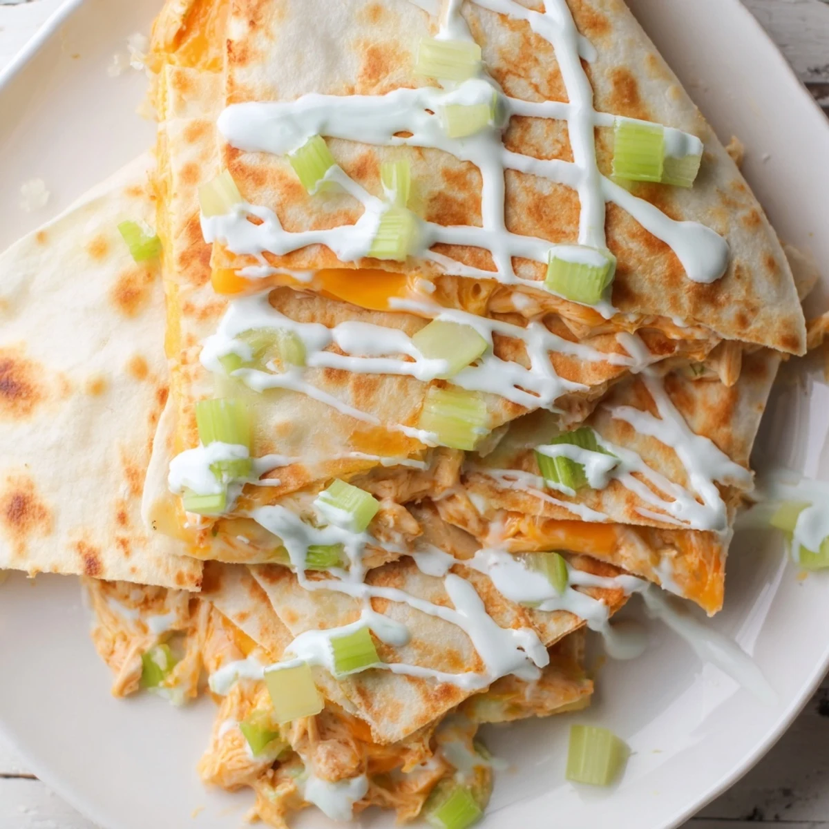 Golden crispy buffalo chicken quesadillas sliced into wedges with creamy white ranch drizzle on top