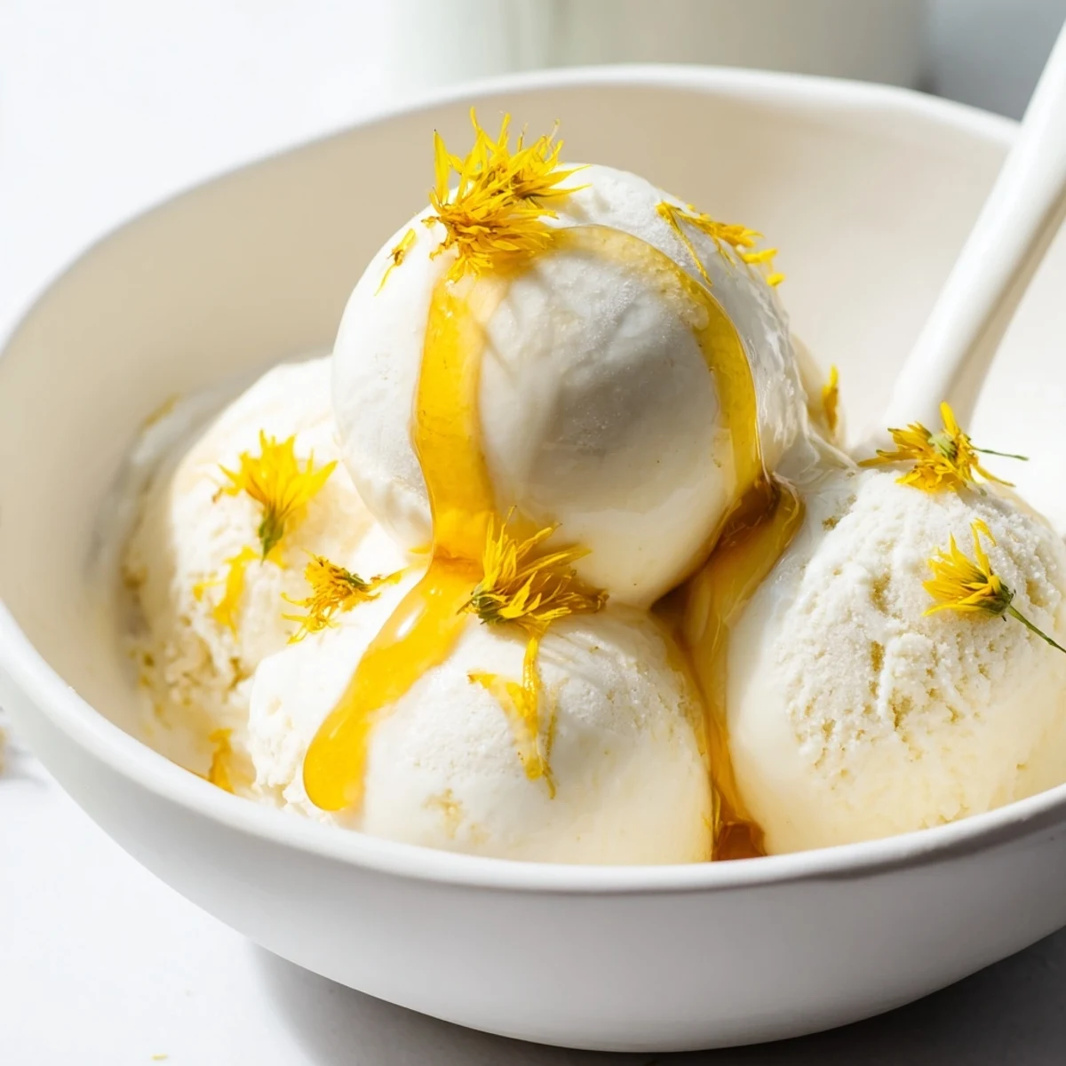 Creamy dandelion honey ice cream scooped into a bowl with golden honey drizzled on top