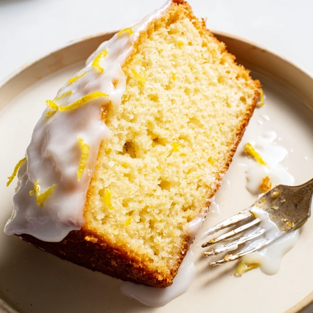 Golden Greek yogurt lemon loaf drizzled with white glaze on a wooden cutting board