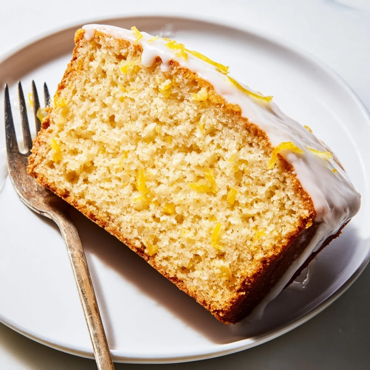 Fresh lemon zest garnishes a tangy Greek yogurt loaf on a white plate